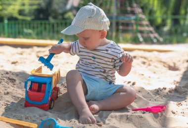 Küçük çocuk kum havuzunda oynuyor, küçük komik Avrupalı çocuk, sarışın, 1,5 yaşında, oyun alanında eğleniyor.