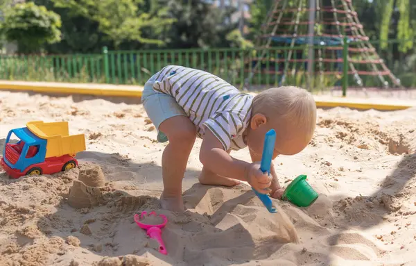 Küçük çocuk kum havuzunda oynuyor, küçük komik Avrupalı çocuk, sarışın, 1,5 yaşında, oyun alanında eğleniyor.