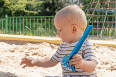 Küçük çocuk kum havuzunda oynuyor, küçük komik Avrupalı çocuk, sarışın, 1,5 yaşında, oyun alanında eğleniyor.