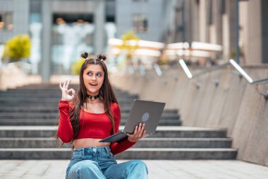 Sokaktaki güzel genç kadın ve bilgisayar laptopu kullanarak çalışıyor.