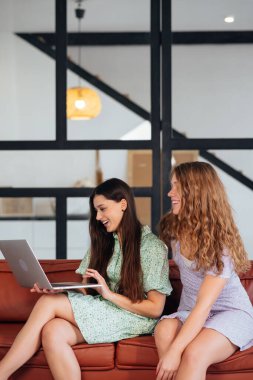 Two young women using computer on couch.