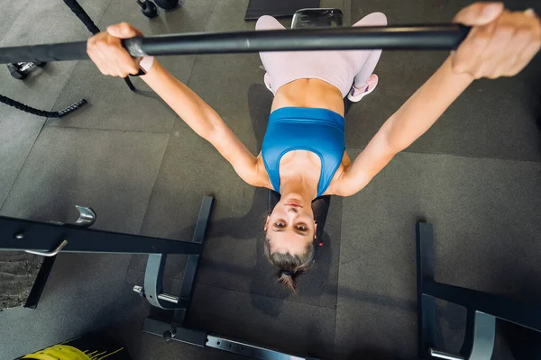 stock image Beautiful woman doing exercises with barbell on a bench press training in a fitness center