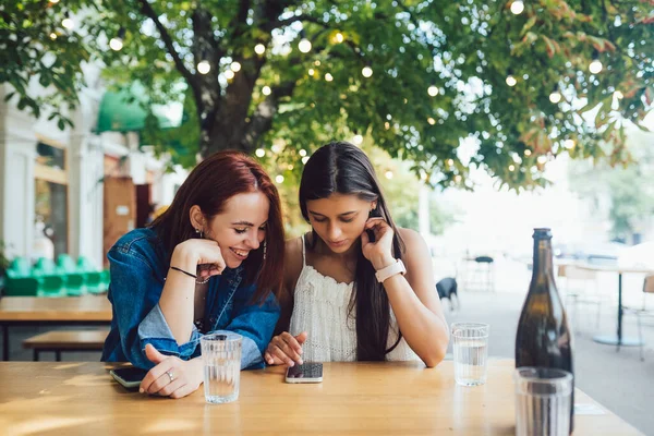 Dwie Przyjaciółki Przeglądające Telefony Komórkowe Siedząc Razem Miejskiej Kawiarni Ulicznej — Zdjęcie stockowe