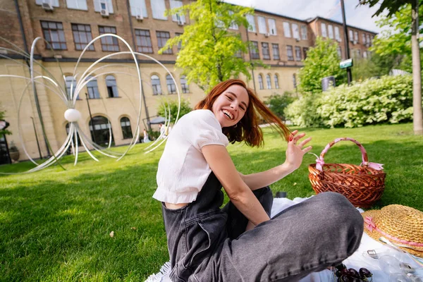 快乐的年轻女子坐在公园草坪上的毛毯上 — 图库照片