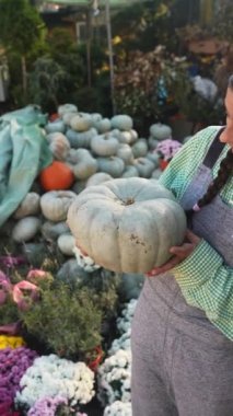 Mutlu dişi çiftçi olgun bir balkabağı tutuyor ve kameraya gösteriyor. Tarım kavramı.