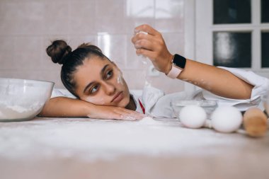 Yorgun genç bir kadın mutfak masasına un döküyor.