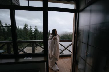 Bir kır evinin balkonunda çay içen genç bir kadın..