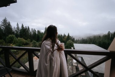 Bir kır evinin balkonunda çay içen genç bir kadın..