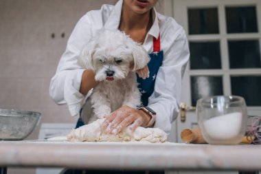 Mutfakta bir kadın mutfakta köpeğiyle hamuru yoğuruyor.