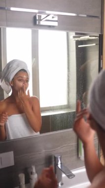 Kafasında havluyla duş alan bir kadın yüzüne nemlendirici sürüyor. Her sabah cilt bakımı yapılıyor..