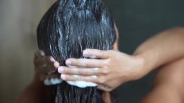 Çekici genç bir kadın banyoda saçını yıkıyor, kameraya arkası dönük duruyor.