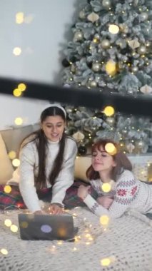 Yeni yıl arifesinde iki genç kadın internette dizüstü bilgisayarda sörf yapıyor.