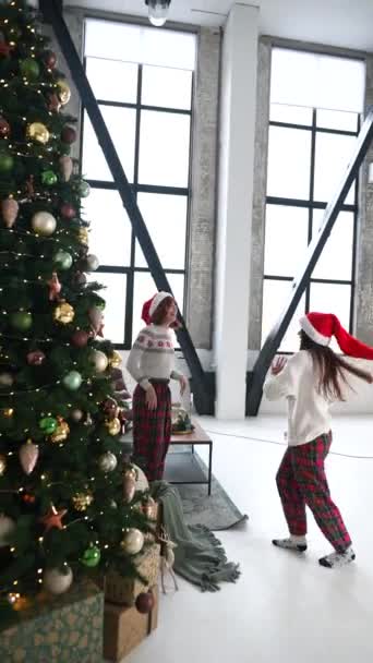 装飾されたリビングルームのスタジオでクリスマスツリーの近くで楽しいダンスをしているクレイジーな若い女性 家で一緒に新年の冬の休日を祝う — ストック動画