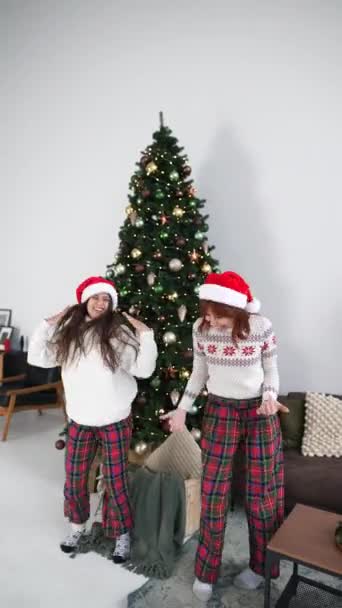 装飾されたリビングルームのスタジオでクリスマスツリーの近くで楽しいダンスをしているクレイジーな若い女性 家で一緒に新年の冬の休日を祝う — ストック動画