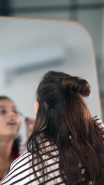 Mutlu genç kadın aynanın önünde yüzüne makyaj yapıyor.