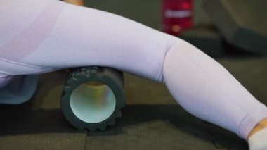 Güzel beyaz kadın sporcu kaslarını germek için köpüklü masaj aleti kullanıyor..