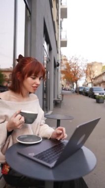 Kahve içerken, bir kadın bir sokak kafesinde dizüstü bilgisayarla çalışır.