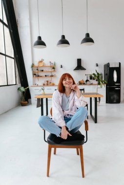 Arka planda modern bir mutfakta sandalyede oturan güzel bir kadının portresi.