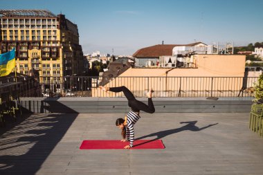 Beautiful young woman working out outdoors and doing yoga handstand exercise on yoga mat