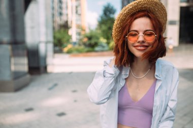 Kızıl saçlı bir kadın sokakta kameraya poz veriyor.