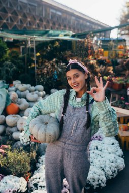 Kot pantolon giyen mutlu çiftçi kadın olgun bir balkabağı tutuyor, sonbahar hasadı. Tarım kavramı.