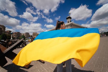 A young woman carries the flag of Ukraine fluttering behind her in the street clipart