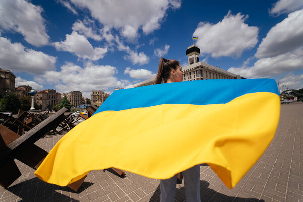 Молодая женщина несет флаг Украины, развевающийся за ней по улице
