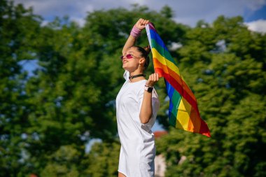 Young woman with lgbt pride flag walking in the park.