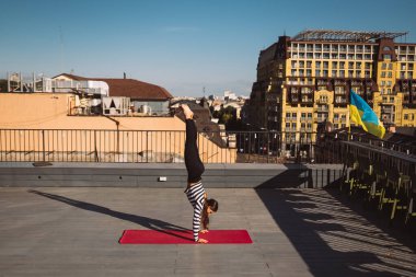 Güzel genç bir kadın dışarıda çalışıyor ve yoga minderi üzerinde yoga amuda kalkıyor.