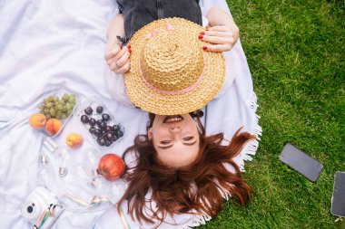 Parktaki çimlerin üzerinde battaniyeye uzanmış mutlu genç bir kadın..