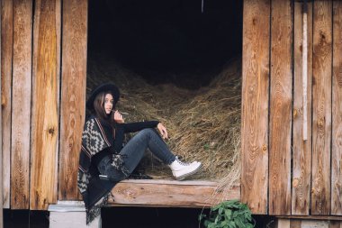 Genç esmer kadın ahırın girişinde otururken poz veriyor. Kırsal biçim.