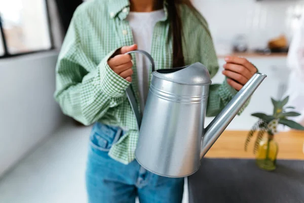 A young woman holds a watering can in her hands at home