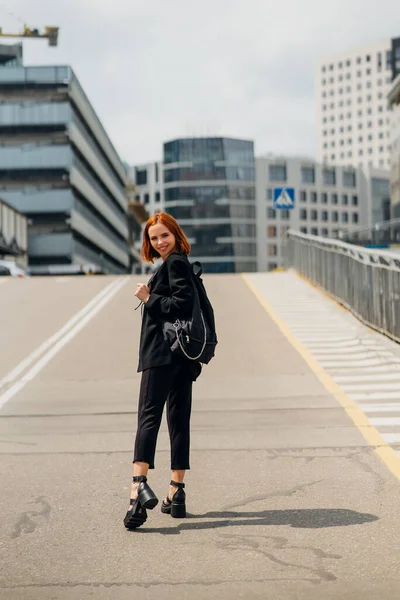 Sırt çantalı, gülümseyen mutlu genç bir kadın yolda dikilirken kameraya poz veriyor.