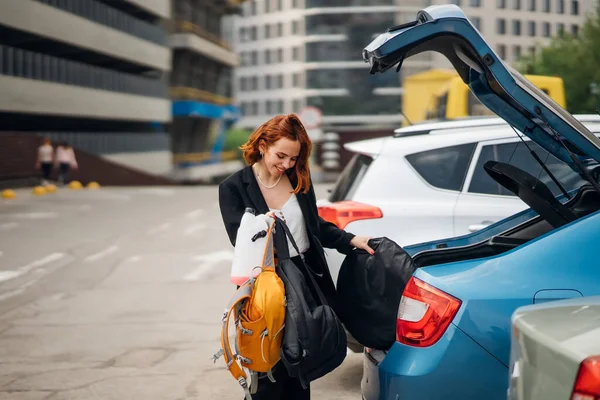 A young woman is packing luggage into the car trunk