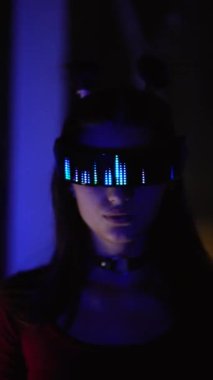 LED gözlüklü, neon ışığı altında duran ciddi bir siber kadın.