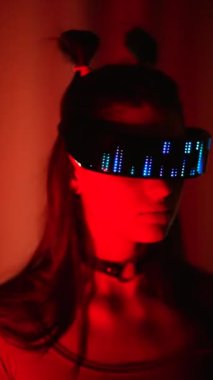 LED gözlüklü, neon ışığı altında duran ciddi bir siber kadın.