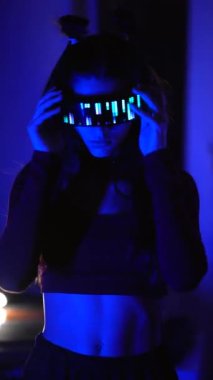 LED gözlüklü, neon ışığı altında duran ciddi bir siber kadın.