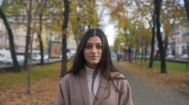 Sonbahar montu giymiş genç bir kadın şehirde bir ara sokakta yürüyor.