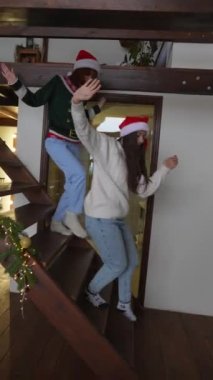 İki genç kadın Noel ağacına koşar ve evdeki hediyelerle sevinir.