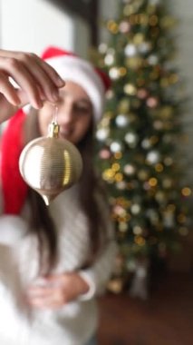 Genç bir kadın topunu gösterip Noel ağacını süslüyor.