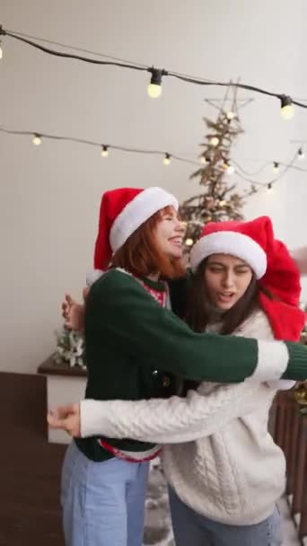 装飾されたスタジオのリビングルームでクリスマスツリーの近くで楽しさと抱擁をしている幸せな若い女性 家で一緒に新年の冬の休日を祝う — ストック動画