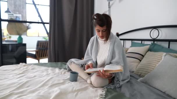 一个年轻的女人坐在卧室的床上看书 — 图库视频影像
