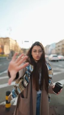 Genç bir kadın şehir caddesinde kameraya konuşuyor.