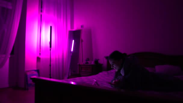 若い女性は夜にベッドの上でスマートフォンでビデオチャットを持っています — ストック動画