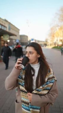 Tasasız genç kadın kahve içiyor. Sokakta yürüyor..