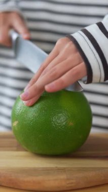 Genç bir kadın mutfakta bir bıçakla meyve kesiyor.