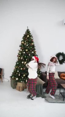 Noel ağacının yanında, dekore edilmiş oturma odasında dans eden aşırı neşeli genç kadınlar. Yılbaşı tatilini evde birlikte kutluyoruz..