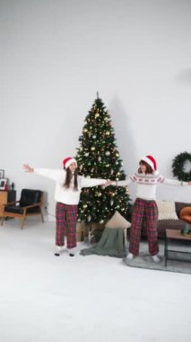 Noel ağacının yanında, dekore edilmiş oturma odasında dans eden aşırı neşeli genç kadınlar. Yılbaşı tatilini evde birlikte kutluyoruz..