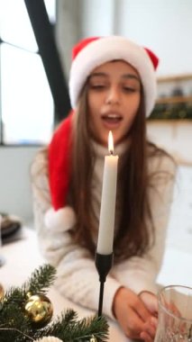 Kırmızı Noel Baba şapkası takan arkadaş canlısı bir kadın mum üflüyor ve bayram sezonunu kutluyor.