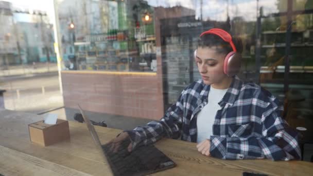 Όμορφο Κορίτσι Ακουστικά Δακτυλογραφεί Στο Laptop Πίσω Από Παράθυρο Στο — Αρχείο Βίντεο
